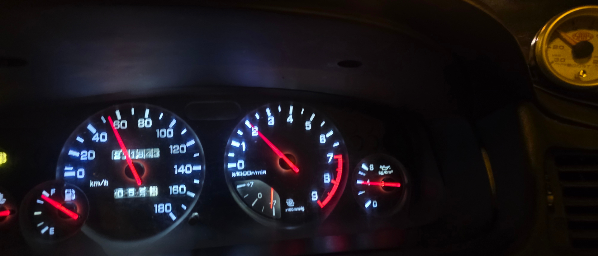 Restored Nissan Skyline gauge cluster lit up at night showing speedometer tachometer and oil pressure gauges
