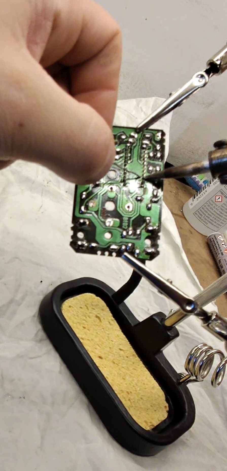 Hand holding Nissan cluster PCB on helping hands station with soldering iron re-flowing joints